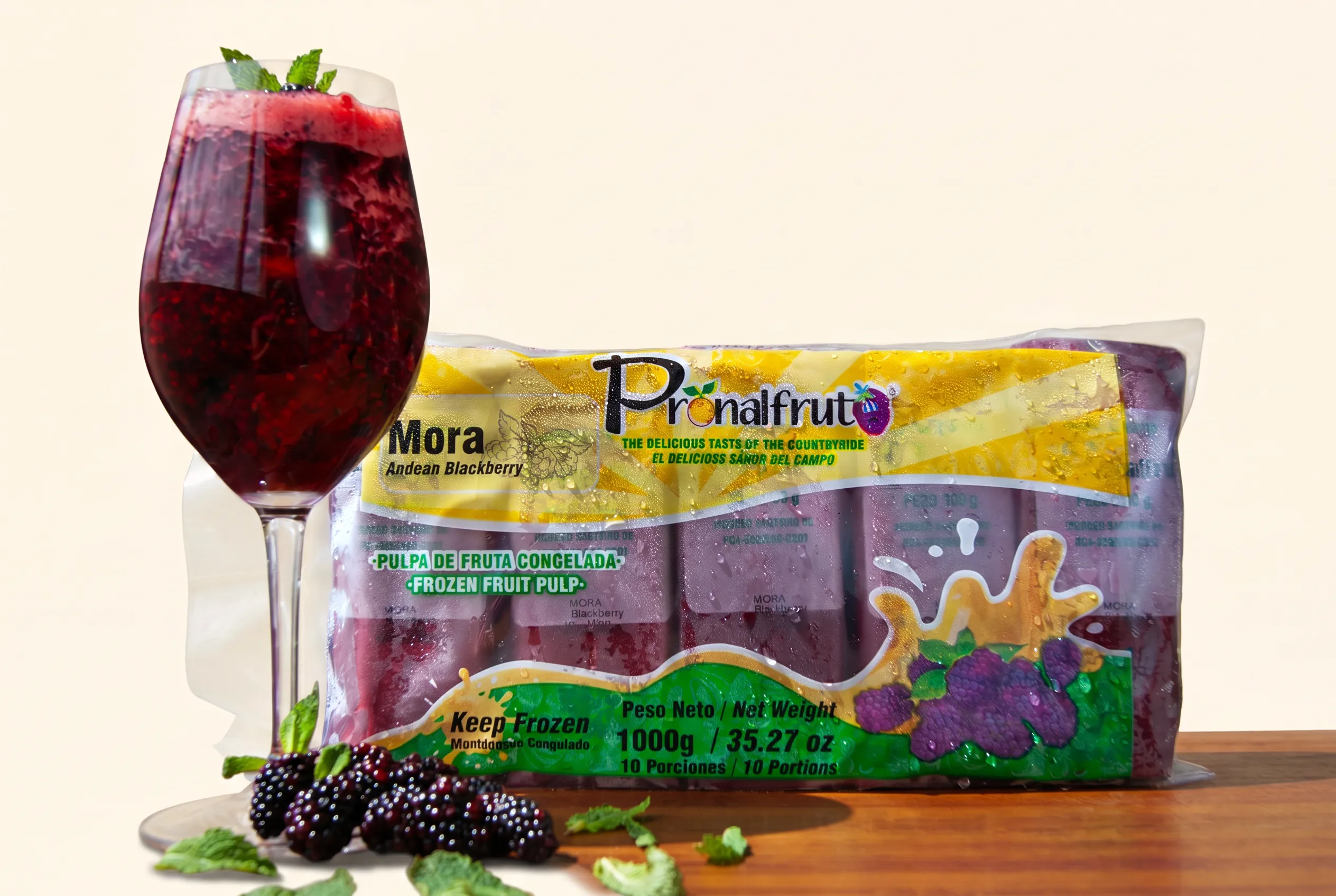 Blackberry smoothie glass next to a Pronalfrut pulp package and fresh blackberries